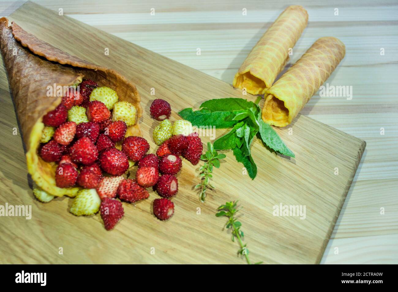 Cono dorato pieno di fragole e tre cialde decorate con menta verde, su sfondo di legno. Colazione per tè o caffè. Cibo Foto Stock
