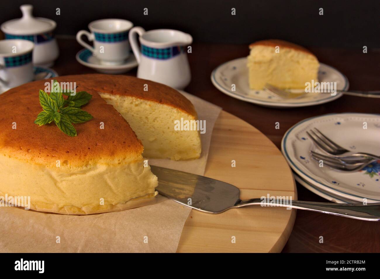 Tabella in cui si vede un cheesecake in stile giapponese accanto a. alcune tazze per tè o caffè Foto Stock