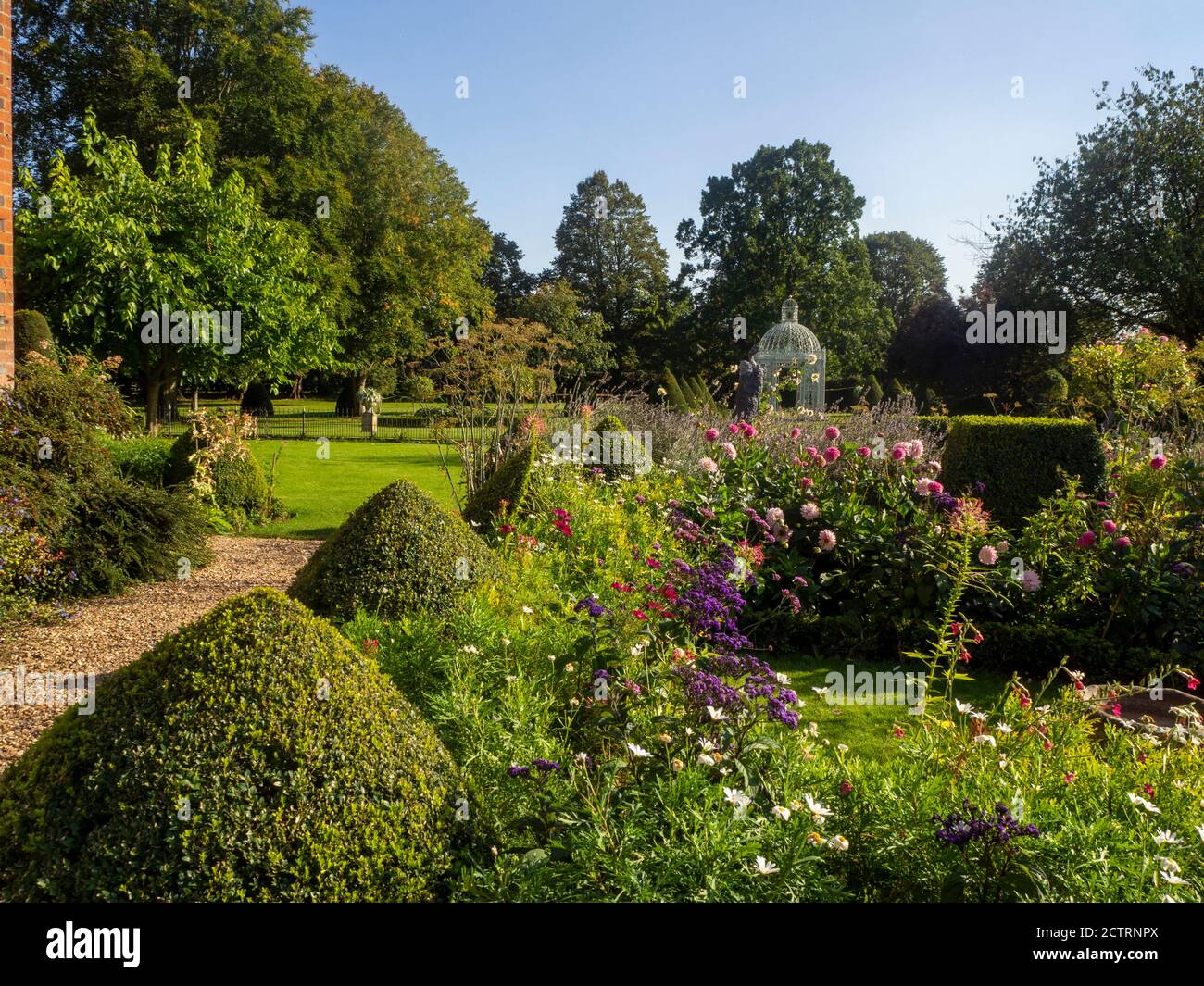 Chenies Manor Garden, bella in tarda estate sole. Topiario a scatola, piante erbacee rosa e blu e dahlias con il Parterre e la Pagoda. Foto Stock