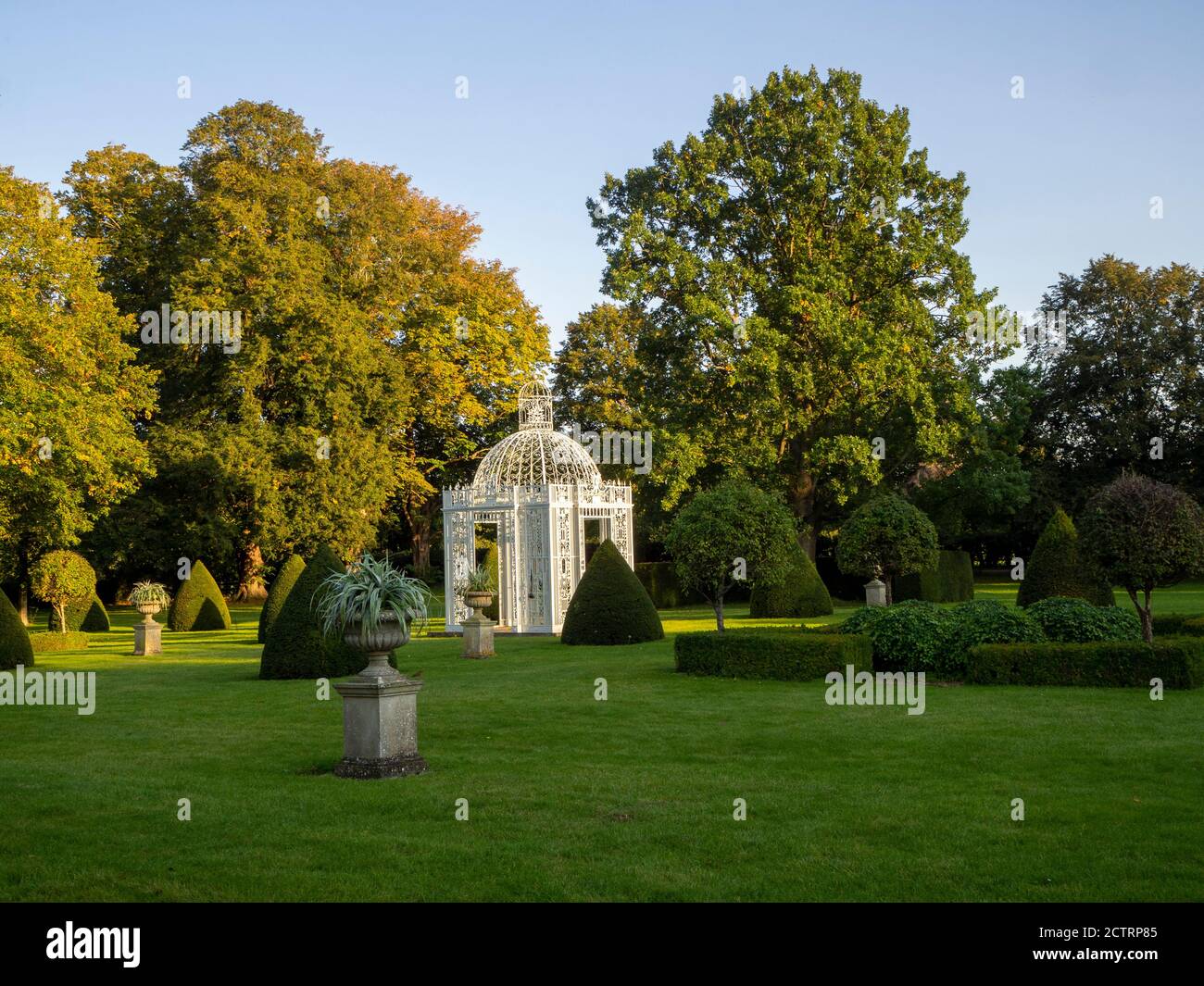 Chenies Manor Parterre a metà settembre 2020. Alberi decidui maturi, pagoda bianca, topiario sul prato con sole e ombra di tardo pomeriggio. Foto Stock