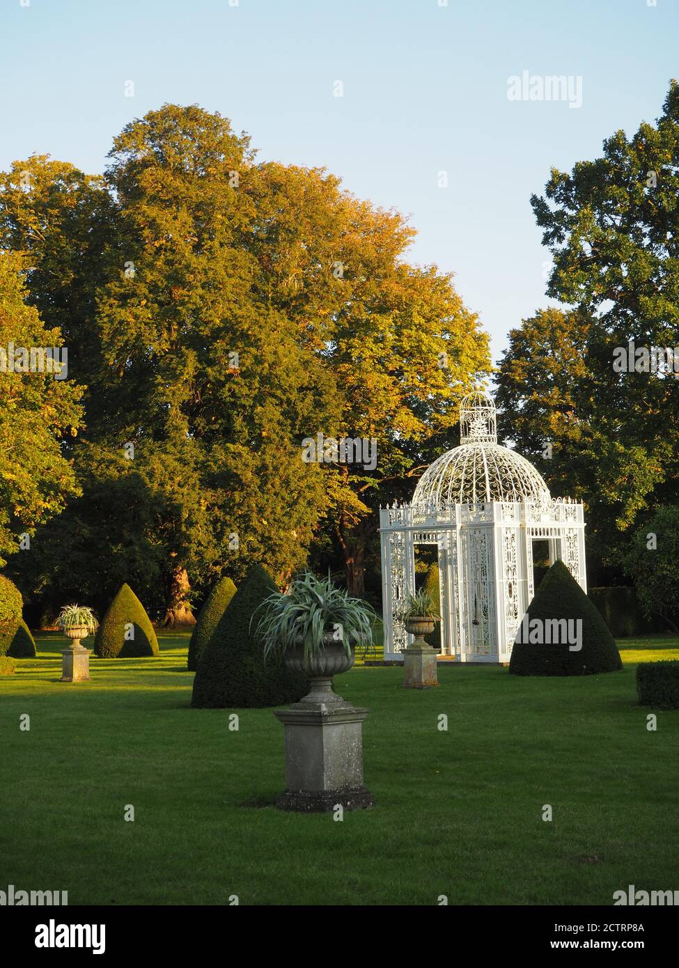 Chenies Manor Parterre a metà settembre 2020. Alberi decidui maturi, pagoda bianca, topiario sul prato con sole e ombra di tardo pomeriggio. Foto Stock