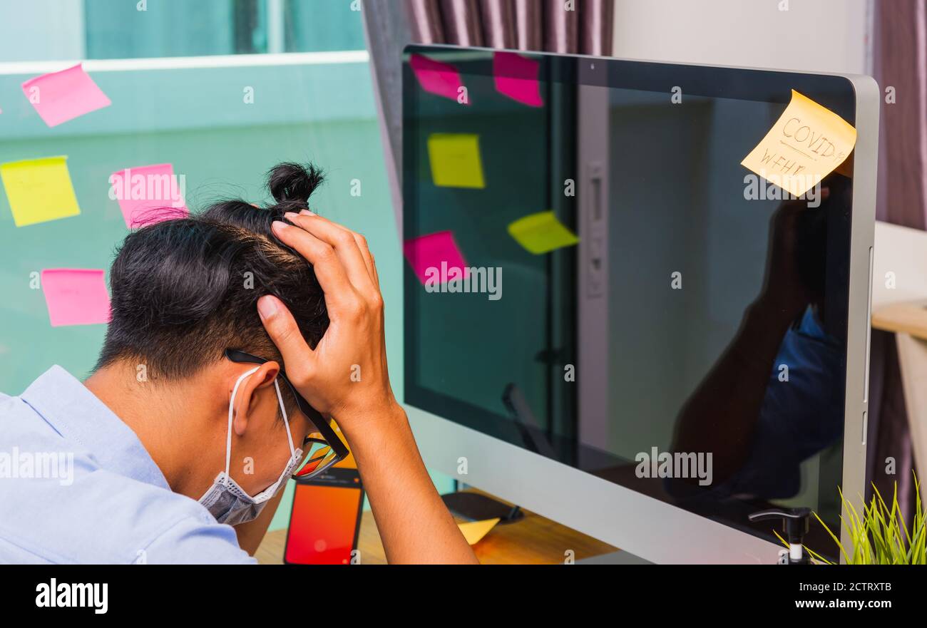 Giovane uomo d'affari stanco che indossa una maschera protettiva con gel disinfettante accanto, lavoro da casa con il computer che stese le mani tenendo templi, Foto Stock