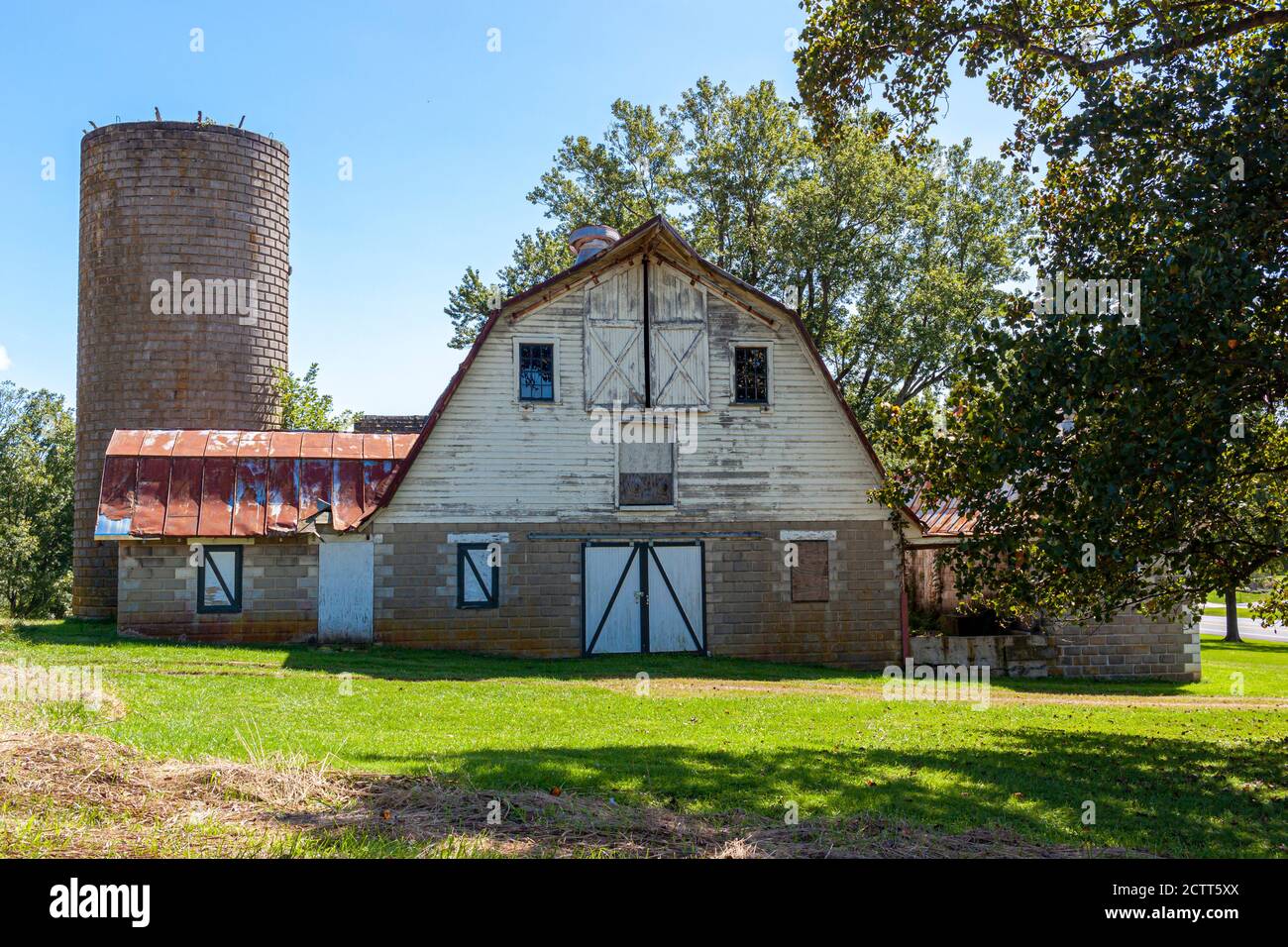 Un'antica casa colonica abbandonata con un alto silo di mattoni e un grande fienile con soffitto di stagno arrugginito. Questo antico complesso di edifici in discesa e' circondato da gr Foto Stock
