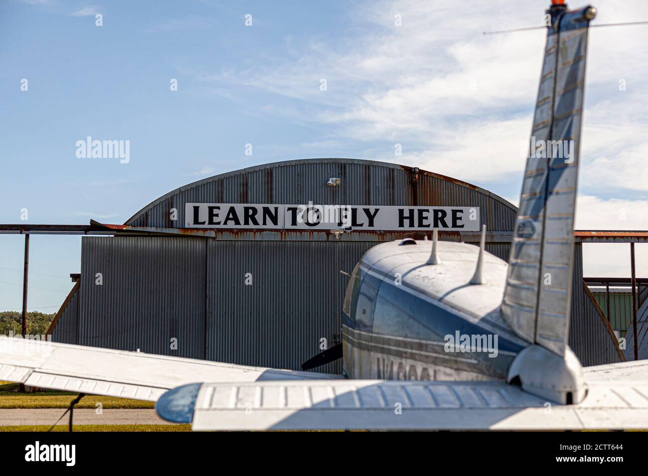 Indian Head, MD, USA 09/19/2020: "Impara a volare qui" in cima a un hangar di aeroporto arrugginito di stagno nel locale aeroporto del Maryland (2w5). Un Piper PA-28 Cherokee Sing Foto Stock
