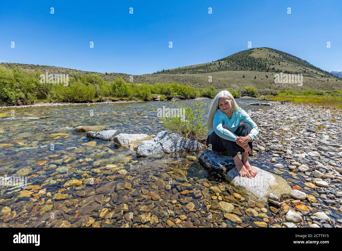 USA, Idaho, Sun Valley, Donna seduta sulla roccia nel fiume Foto Stock