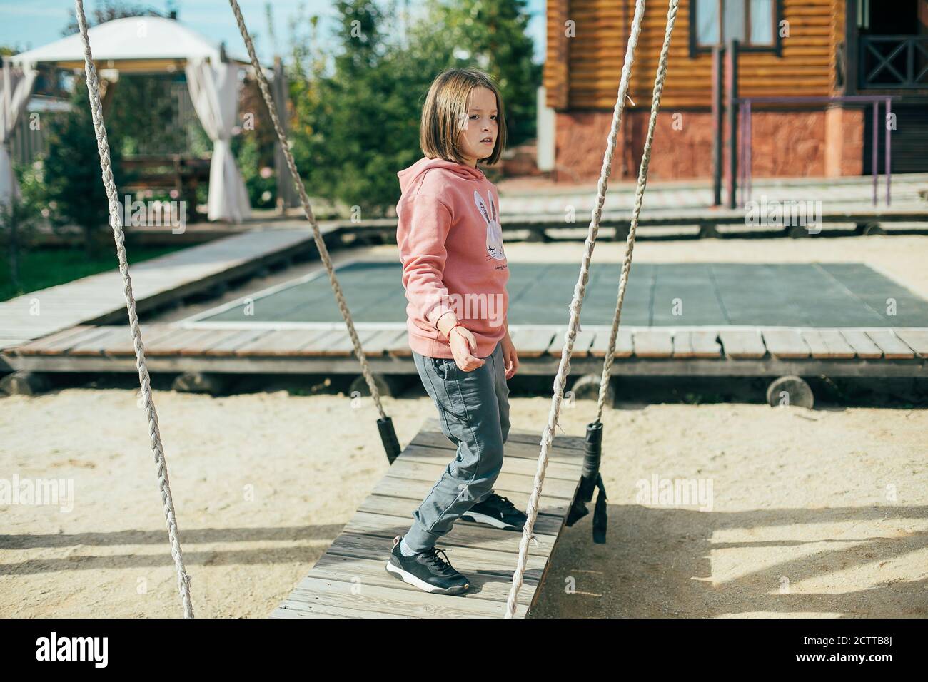Carina caucasica ragazza 7-8 anni in una felpa rosa e pantaloni grigi sul parco giochi nel parco cittadino. Attività all'aperto, stile di vita, leisù per bambini Foto Stock