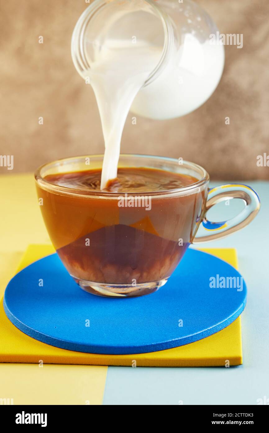 Una tazza di caffè e latte che scorre in una tazza su un podio giallo e blu. Foto Stock