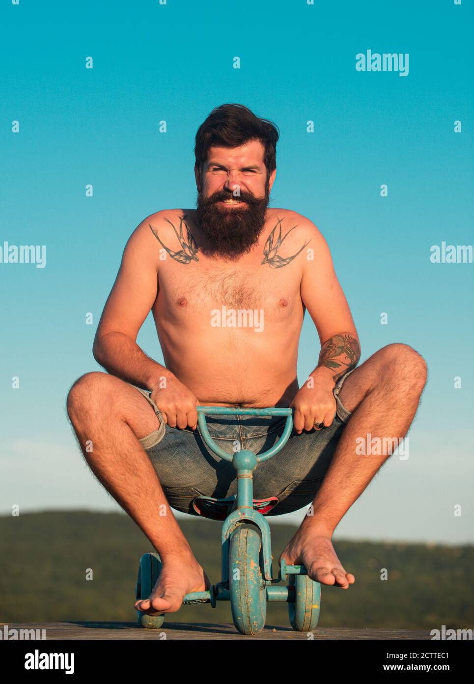 Ragazzo che cavalcano i bambini triciclo. Uomo divertente in bicicletta. Un pazzo emozionale su una moto per bambini. Foto Stock