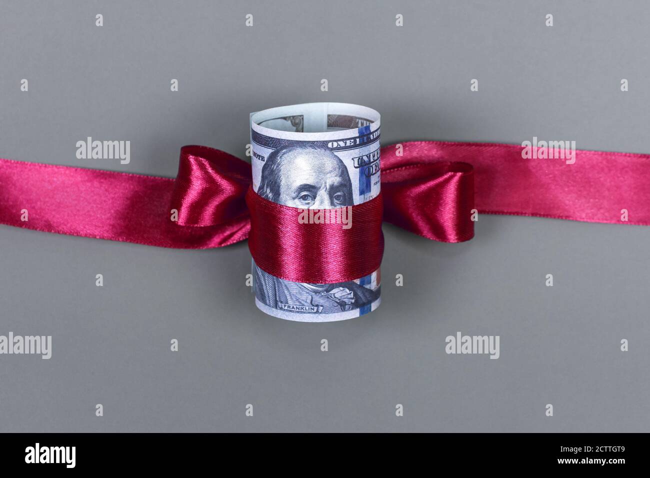 Centinaia di dollari legati con arco rosso su sfondo grigio. Denaro, regalo avvolto in arco rosso e nastro, valuta americana, contanti, successo aziendale, bonus Foto Stock