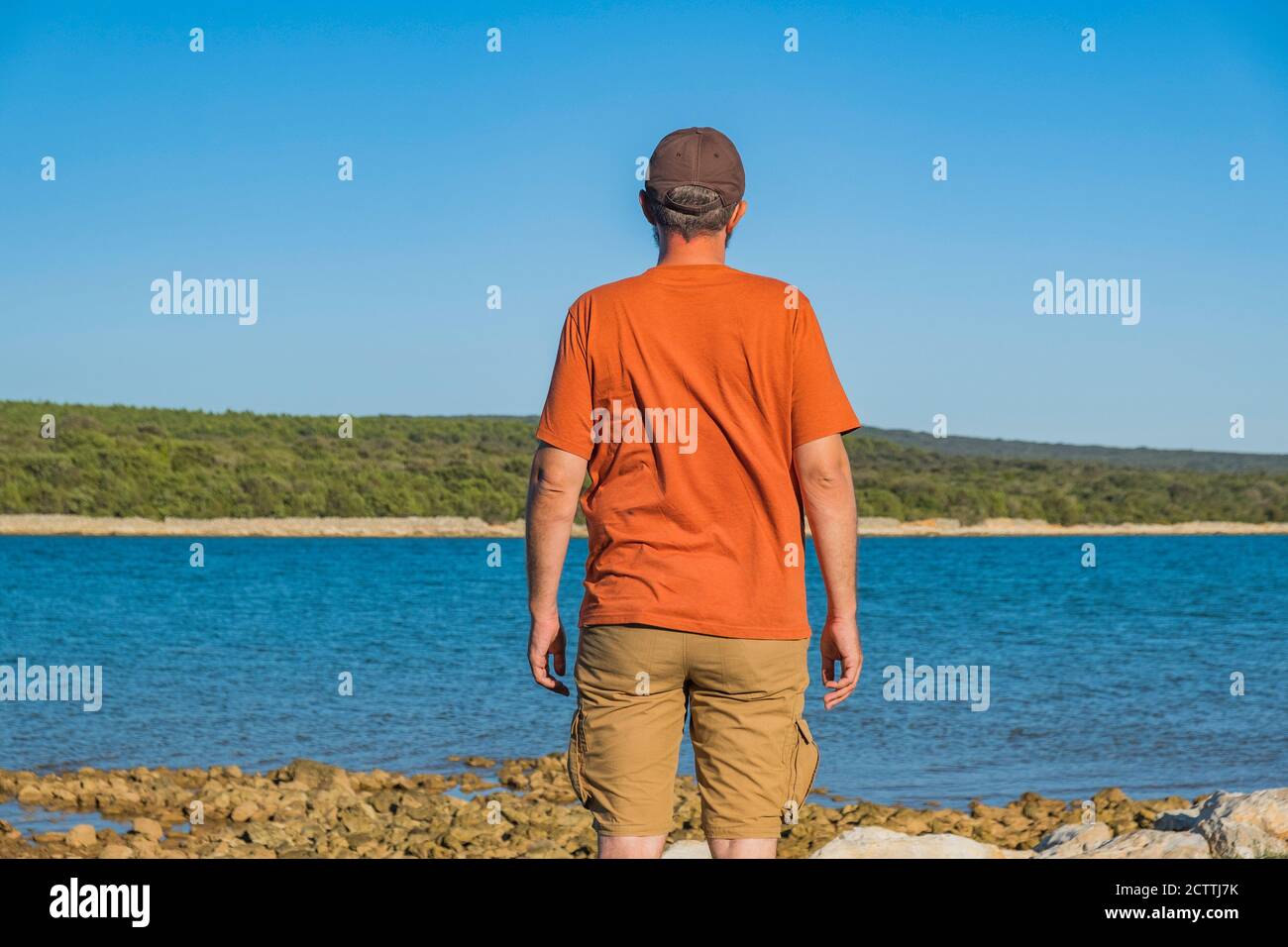 Uomo in pantaloni cargo in piedi sulla riva del mare e osservando la superficie, isola di Lussino, Croazia Foto Stock
