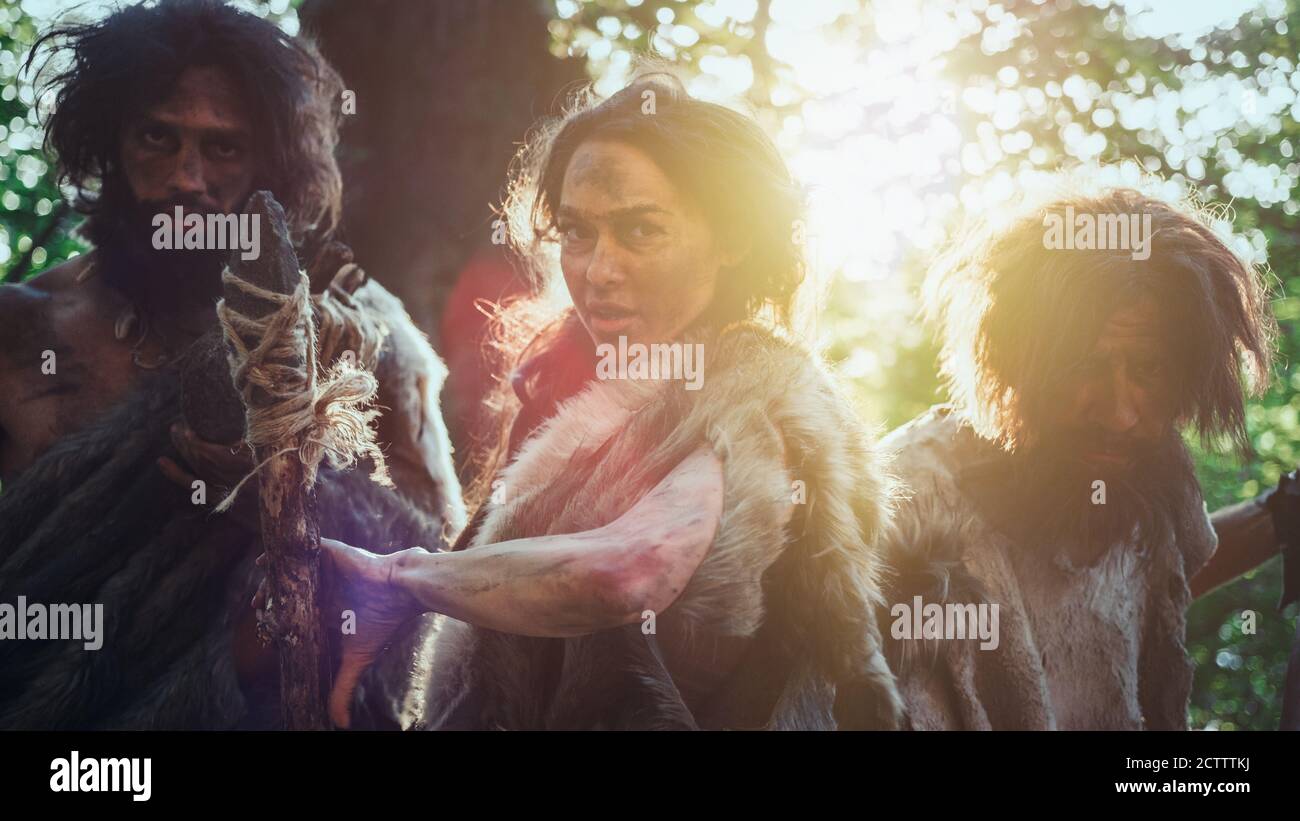 Leader femminile e due Guerrieri Cavemen Primeval minaccia Enemy con la pietra punta Spear, Scream, Defending loro Grotta e territorio nella preistoria Foto Stock