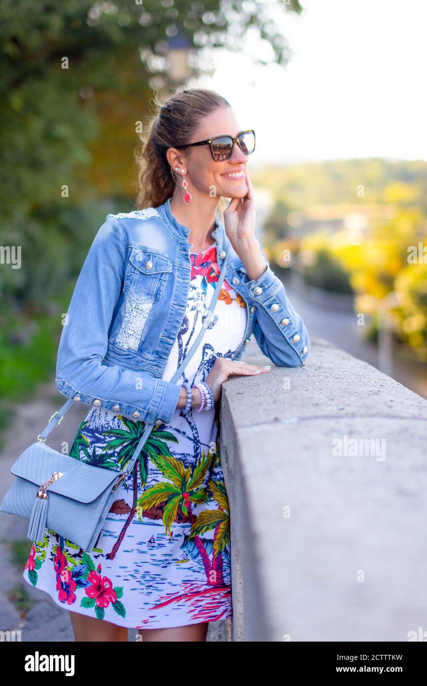 Felice donna allegra nel parco che si inchinava alla ringhiera di pietra, sorrido Foto Stock