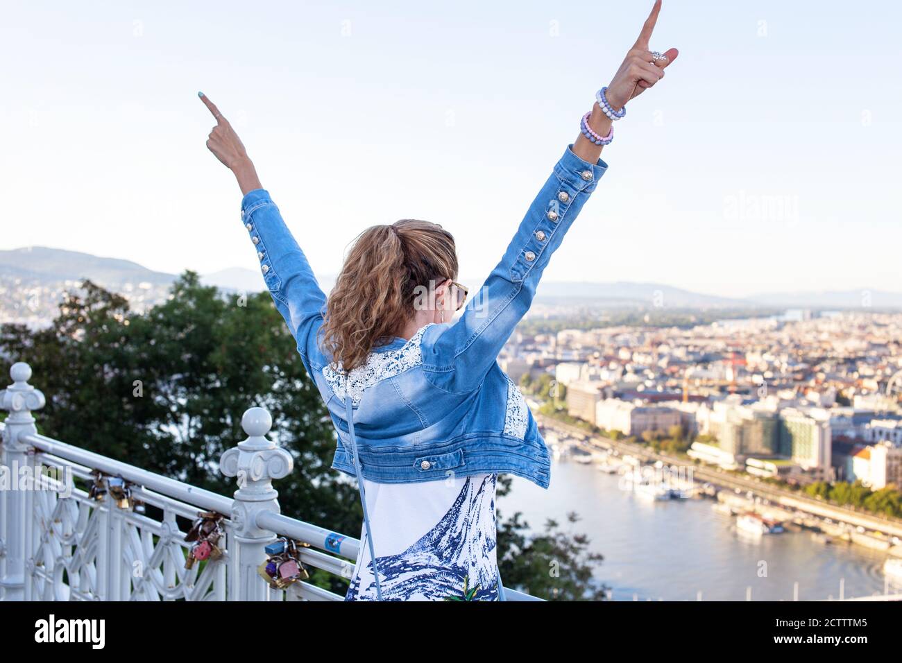 Giovane donna urbana braccia alzando al panorama della città, vista posteriore Foto Stock