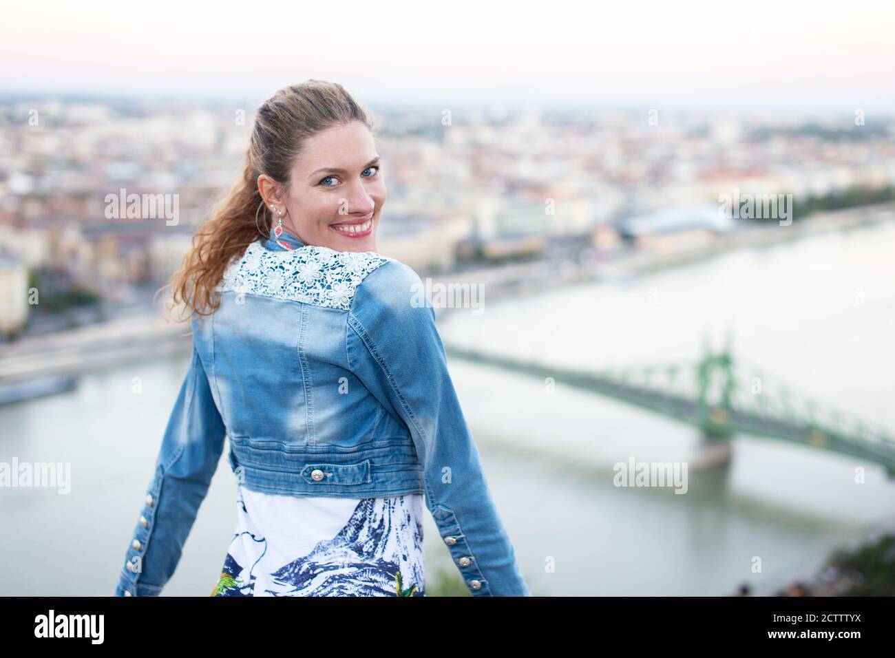 Felice giovane donna che guarda indietro durante il viaggio a Budapest, Danubio con Ponte della libertà, Ungheria Foto Stock