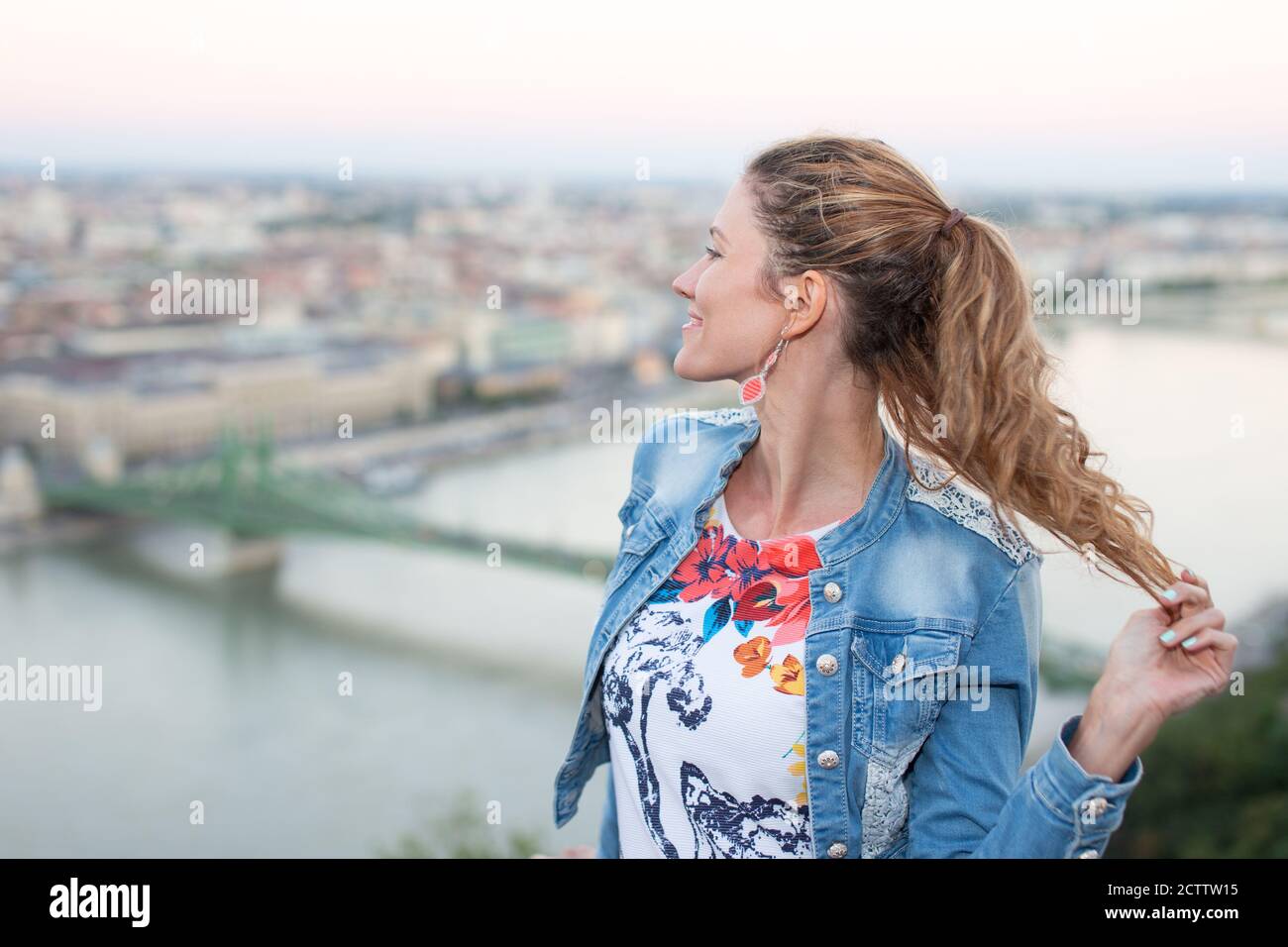 Happy 30s donna urbana che tiene i capelli nel panorama di Budapest, Ungheria Foto Stock