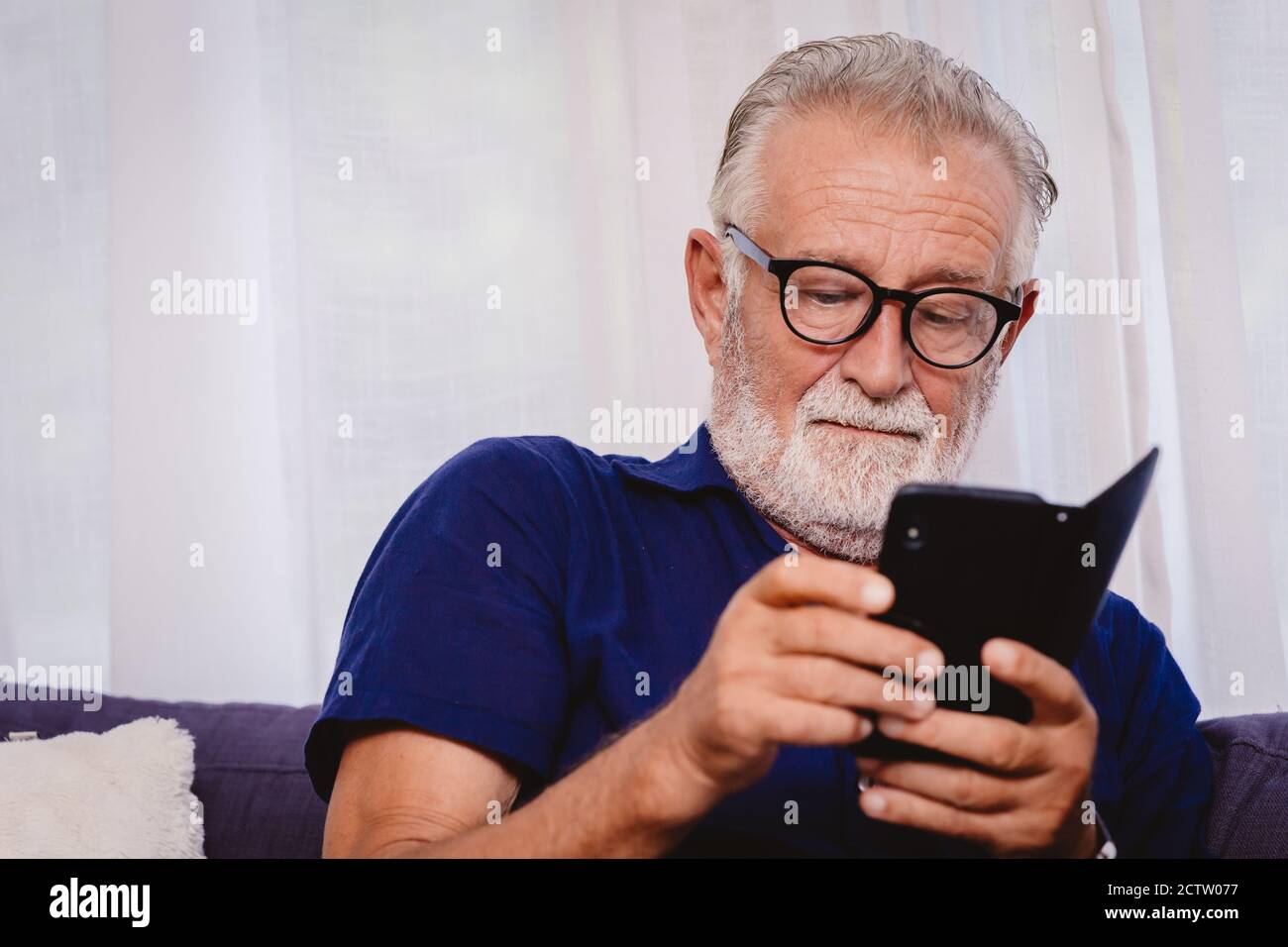 uomo anziano che guarda lo smartphone per leggere gli aggiornamenti delle notizie o per giocare alle app dei social network. Foto Stock