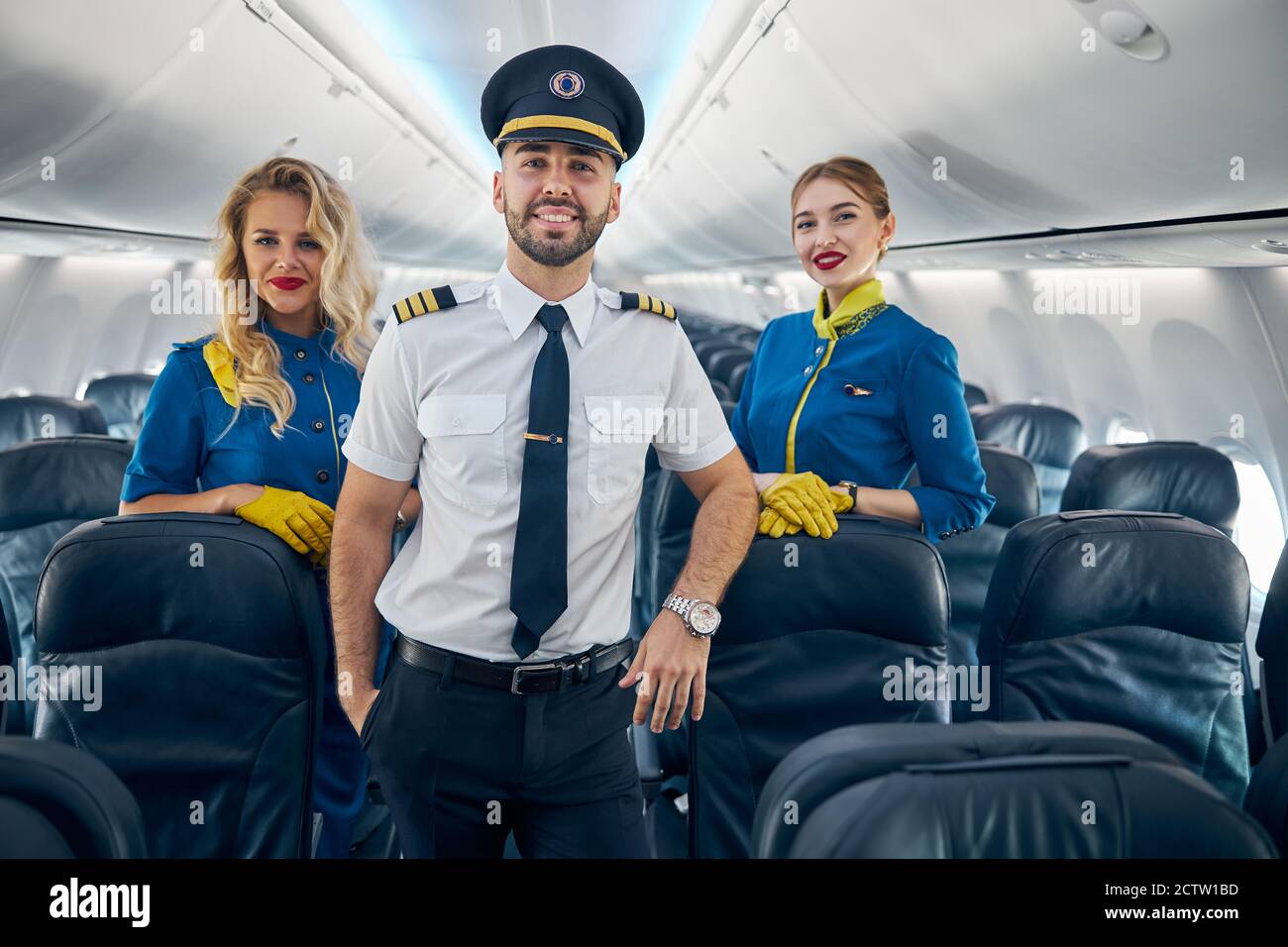 Felice sorridente bel pilota con due hostess aria sul asse di aereo Foto Stock