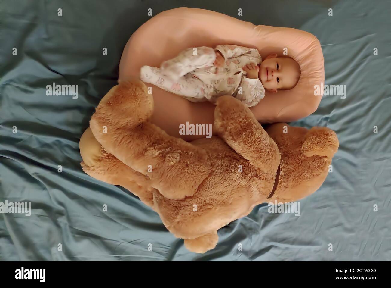 Il bambino neonato felice si trova in un bozzolo speciale, un materasso ortopedico vicino al grande e morbido orso giocattolo Foto Stock