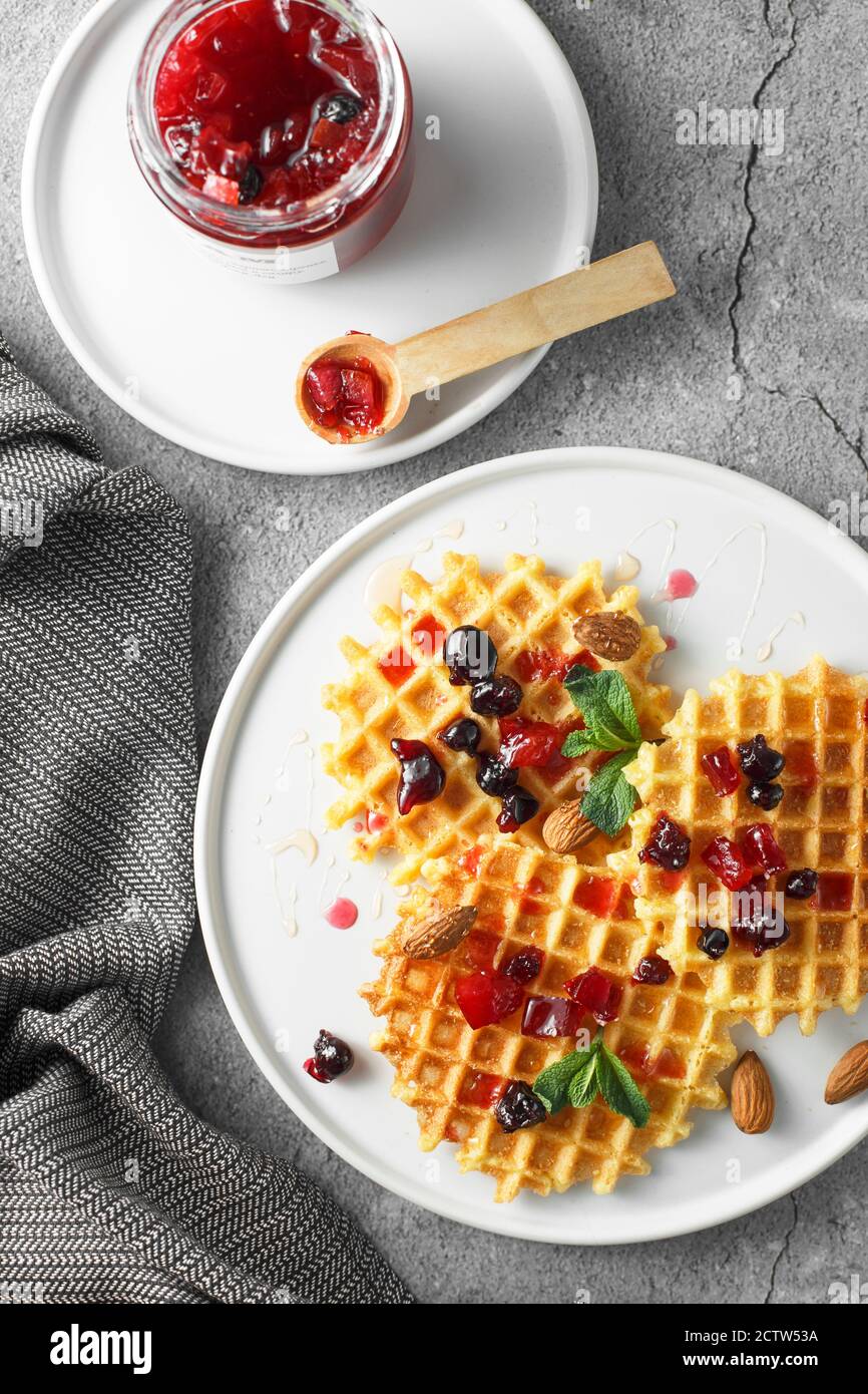 Piatto con marmellata di pompelmo con vassoio di frutti di bosco. Vasetto di marmellata d'arancia e cialde viennesi su fondo grigio in cemento. Pho da cucina top-down Foto Stock