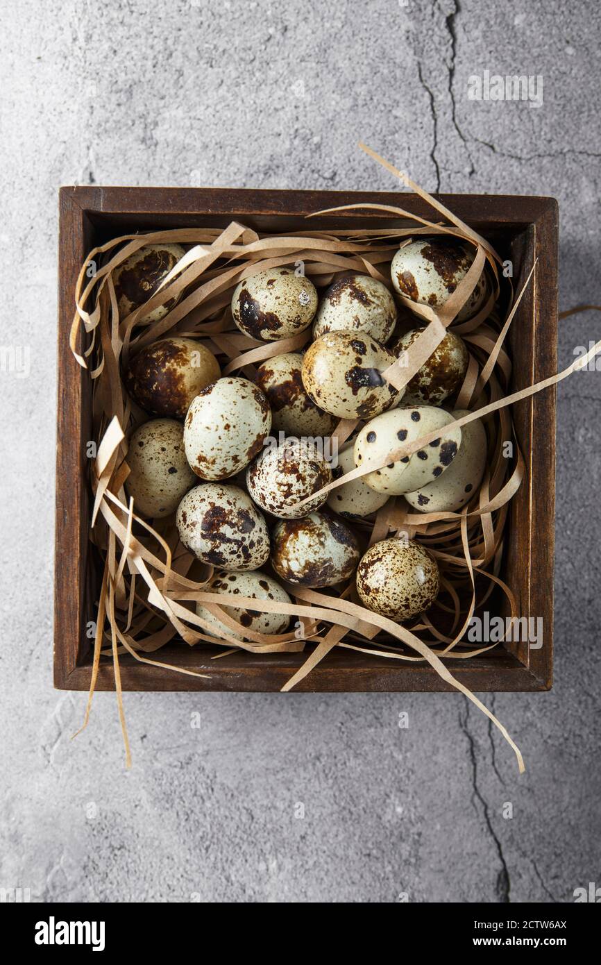 Uova di quaglia. Composizione piatta con uova di quaglia nella scatola di legno sullo sfondo di calcestruzzo. Un uovo rotto con un tuorlo luminoso. Fattoria uova Quail Foto Stock