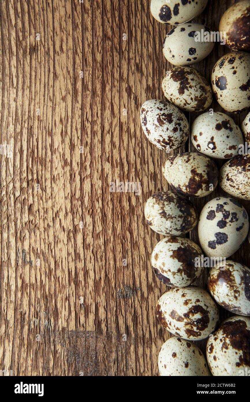 Uova di quaglia. Composizione piatta con piccole uova di quaglia sullo sfondo naturale di legno. Un uovo rotto con un tuorlo luminoso. Fattoria uova Quail Foto Stock