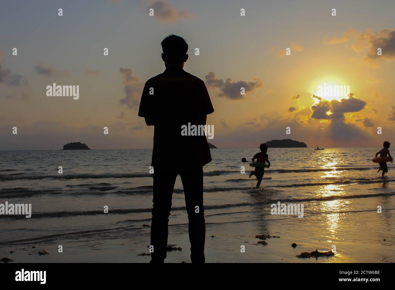 L'uomo solitario si erge sulla spiaggia guarda verso la luce del sole, scalini sulla sabbia, tramonto, silhouette di persona che cammina sulla spiaggia di mare. Foto Stock