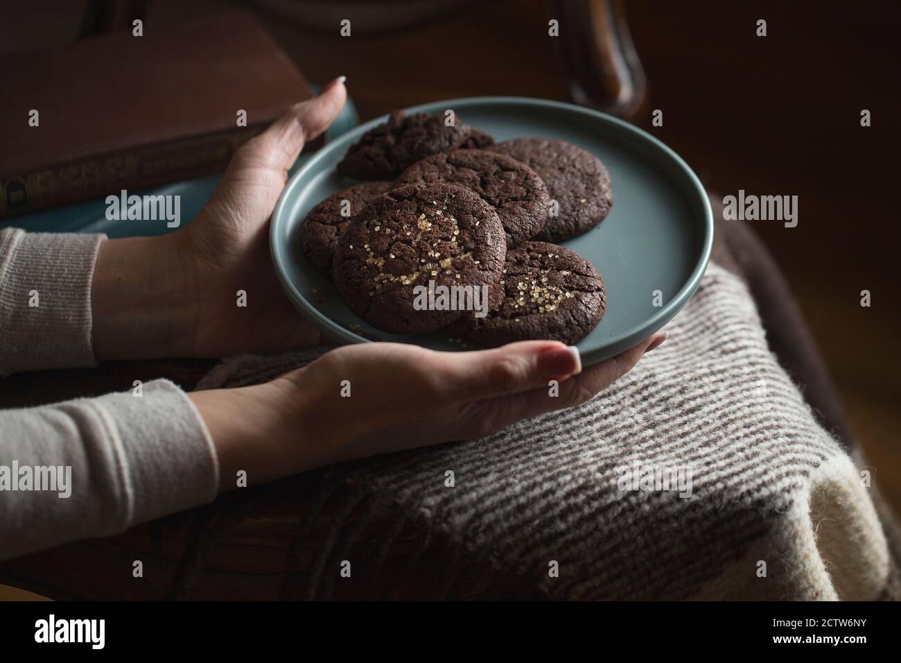 Biscotti al cioccolato sul piatto. Dark and Moody, Mystic Light fotografia alimentare. Mani femminili che tengono un piatto di biscotti di chip di cioccolato. Foto Stock