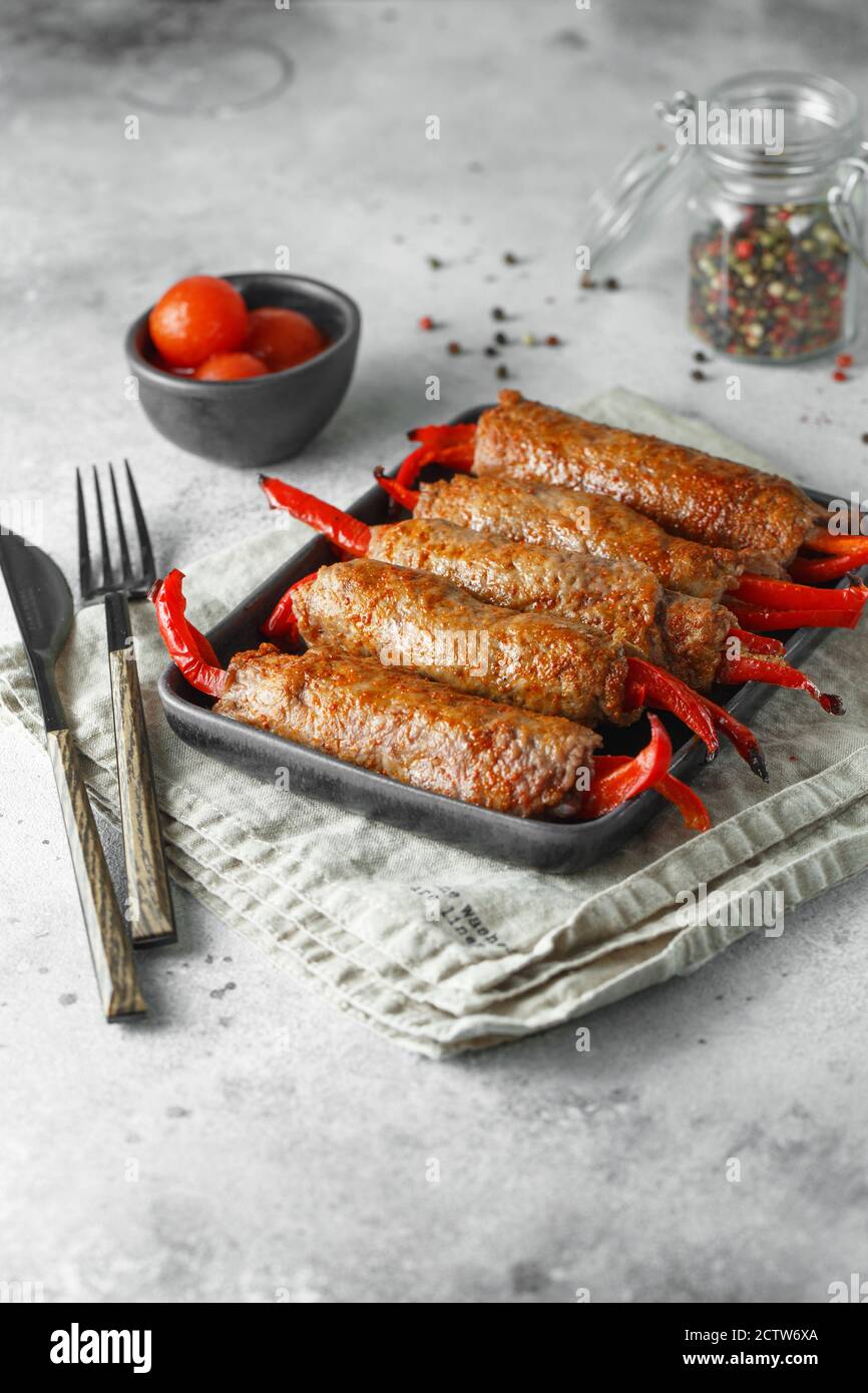 Involtini di carne ripieni di paprika rossa dolce in nero resistente al calore piatto su sfondo grigio Foto Stock