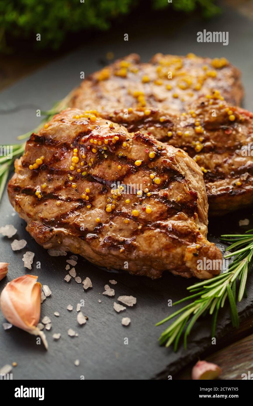 Bistecche di manzo alla griglia con spezie. Pasto pronto per la cena su sfondo di pietra scuro Foto Stock