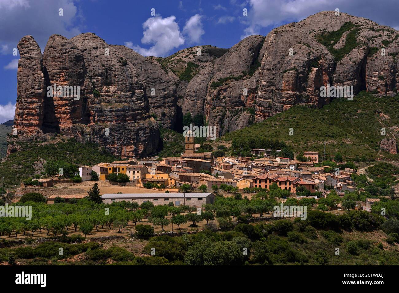 Agüero, un piccolo villaggio ai piedi dei Pirenei a Huesca, Aragona, Spagna, si aggira intorno ad una bella chiesa romanica del 13 ° secolo e si accoccola sotto Los Mallos de Agüero (i Mallets o Ninepins di Agüero). Questa spettacolare formazione, conosciuta anche come le colline di Syncline, è costituita da una roccia conglomerata di epoca terziaria erosa dalle tinte rosse che sale fino a 900 piedi / 275 metri sopra l'insediamento. Foto Stock