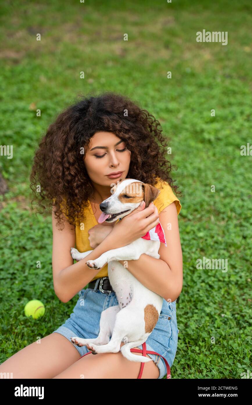 Fuoco selettivo della giovane donna che siede e che tiene il cane sopra erba Foto Stock