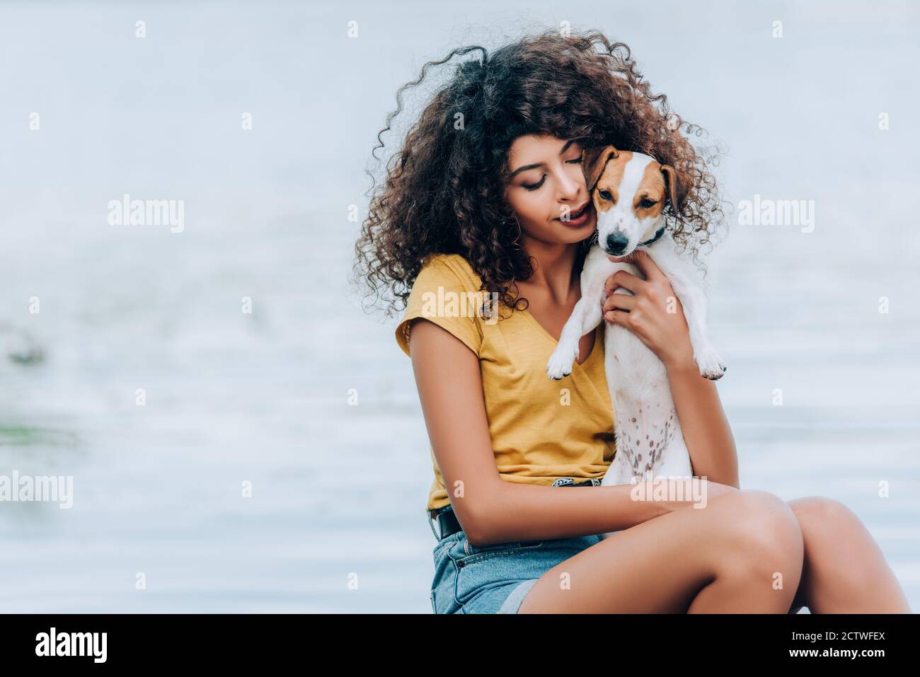 curly donna in estate vestito hugging jack russell terrier cane vicino al lago Foto Stock