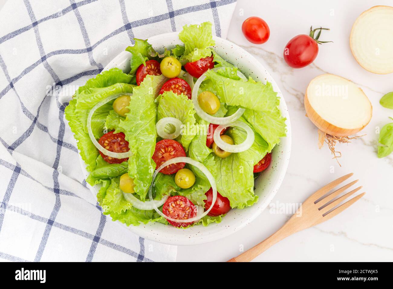 Insalata fresca e sana con lattuga, cipolla, pomodori ciliegini e olive in una ciotola. Cucina mediterranea Foto Stock