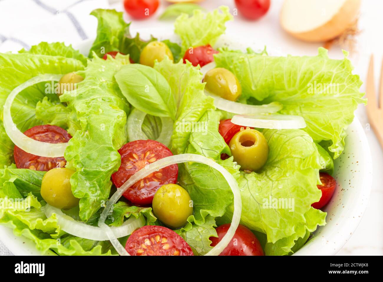 Primo piano di un'insalata fresca e sana con lattuga, cipolla, pomodori ciliegini e olive in una ciotola. Cucina mediterranea Foto Stock