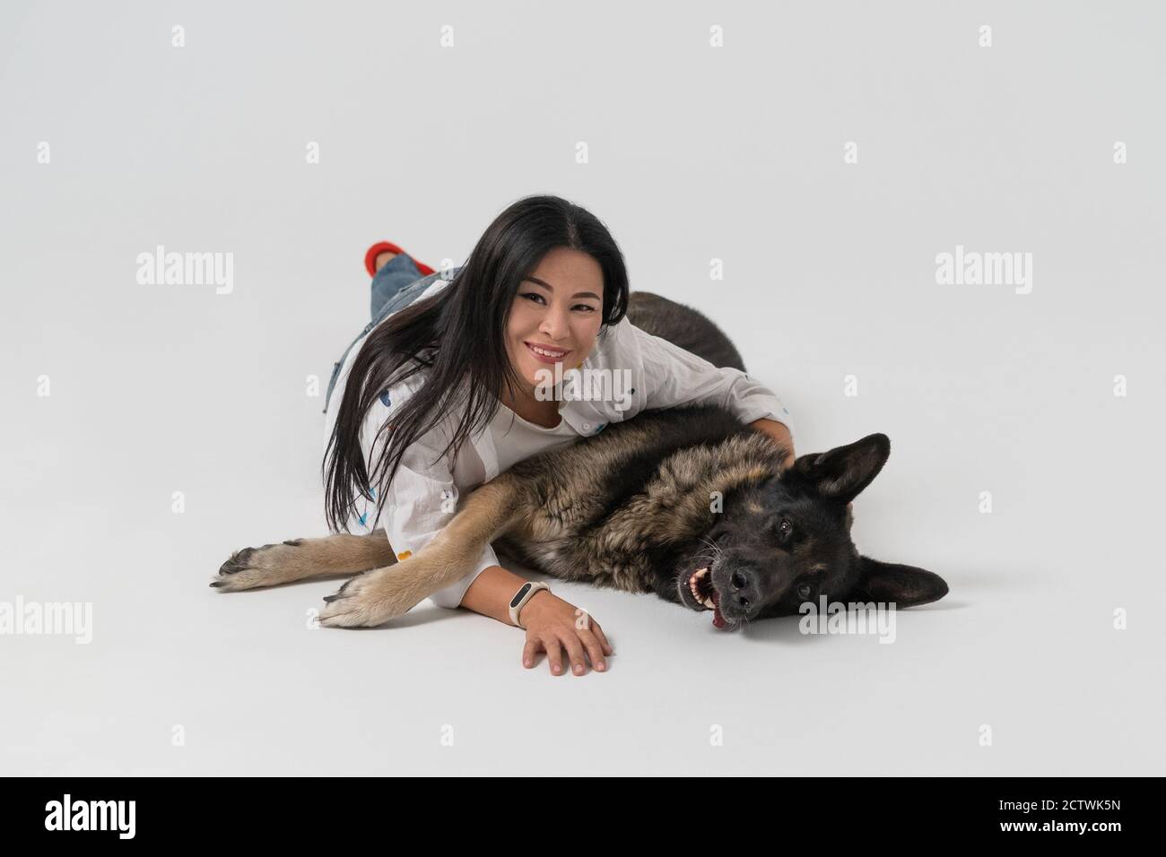 La donna asiatica si trova con un cane da pastore al piano dello studio. Il proprietario abbracca il cane su uno sfondo isolato. La donna guarda nella macchina fotografica e sorride. Alta Foto Stock