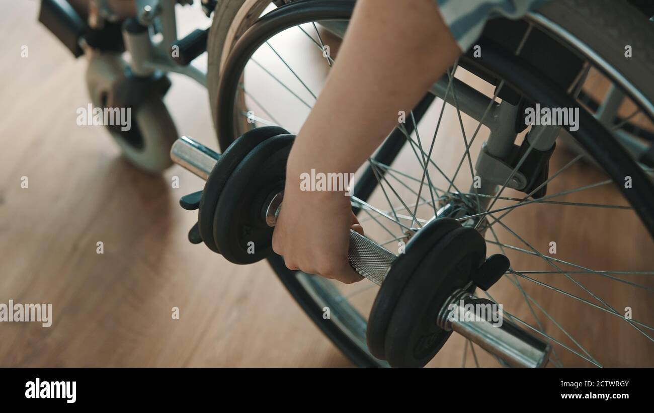 Primo piano di una giovane donna che solleva i pesi mentre si siede in sedia a rotelle. Disabilità e benessere. Foto di alta qualità Foto Stock