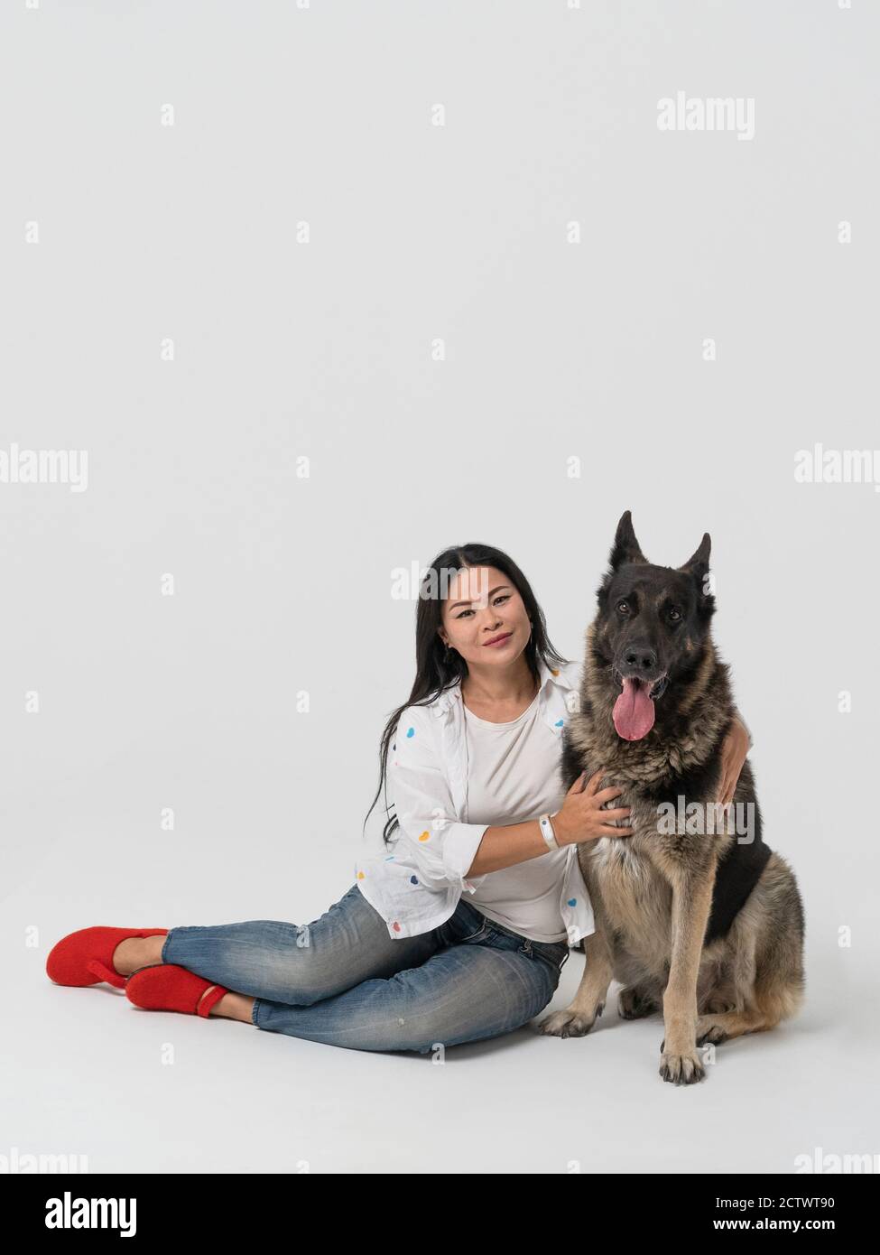 La proprietaria femminile e il cane grande si siedono sul pavimento. Donna asiatica con un Pastore dell'Europa orientale purosangue in uno studio su uno sfondo isolato. Alta Foto Stock