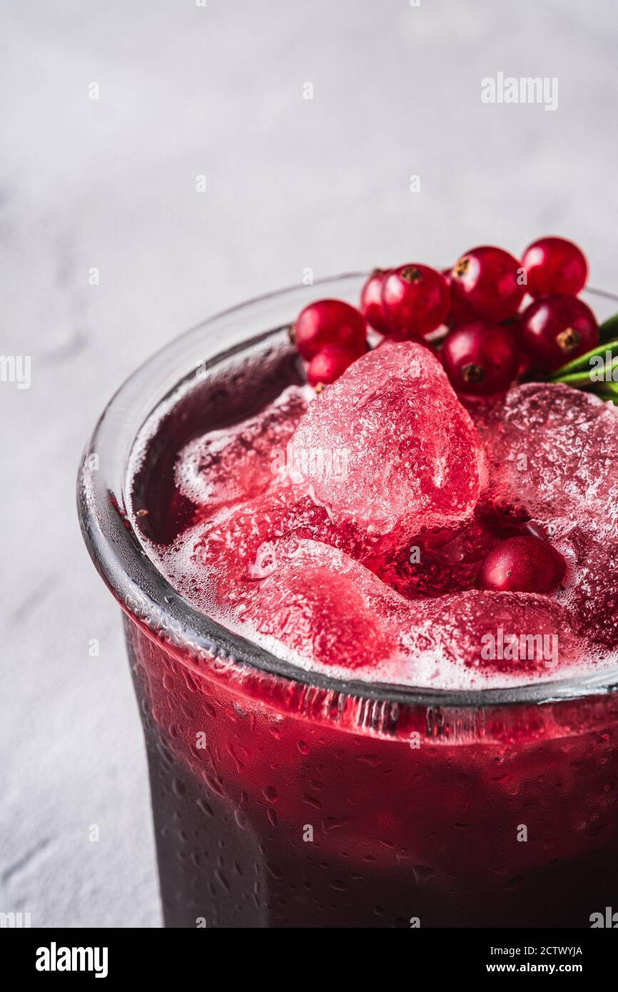 Fresco ghiaccio freddo frutta cocktail in vetro, rinfrescante estate rosso ribes bacca bevanda con foglia di rosmarino su fondo di pietra cemento, angolo vista macro Foto Stock