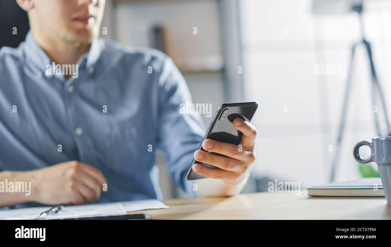 Imprenditore seduto alla sua scrivania lavora con documenti nell'ufficio elegante, utilizzando smartphone, utilizza Social Media App, e-mail Business Partners Foto Stock