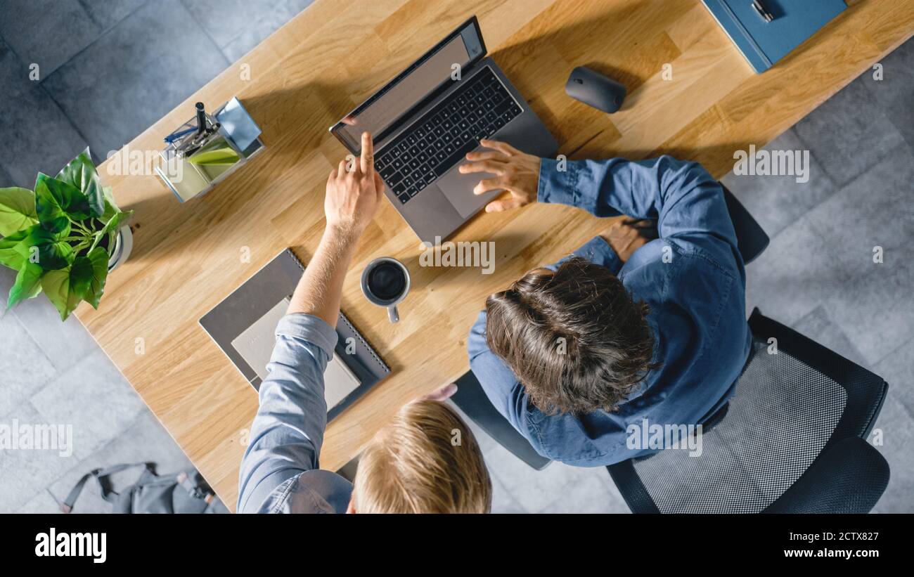 Top View Shot di un giovane uomo d'affari che lavora alla sua scrivania su un laptop, parla con il suo Manager e ascolta un consiglio sul concetto di progetto. Due uomini Foto Stock