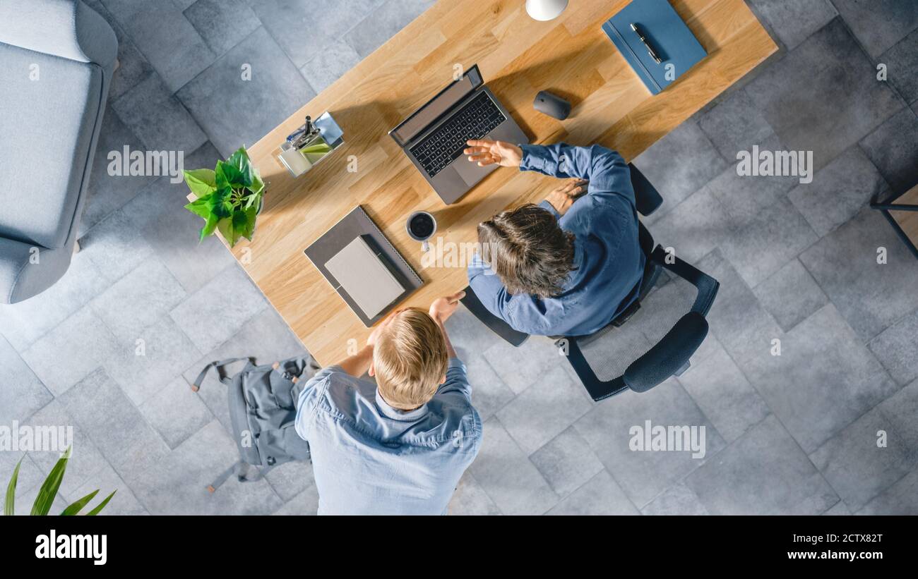 Top View Shot di un giovane uomo d'affari che lavora alla sua scrivania su un laptop, parla con il suo Manager e ascolta un consiglio sul concetto di progetto. Due uomini Foto Stock