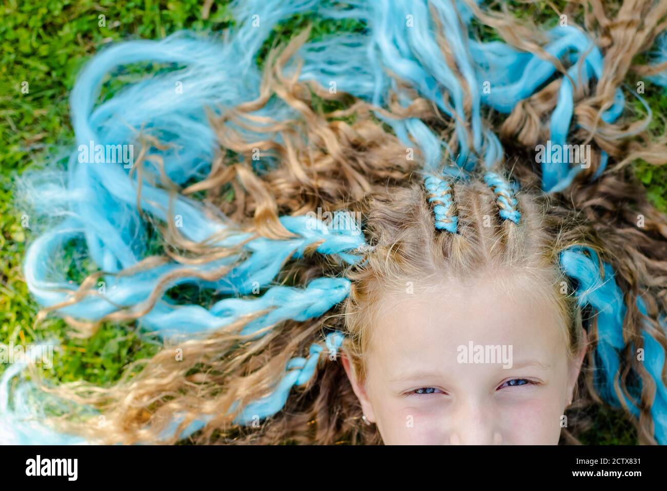 Ritratto di bella ragazza con molte trecce con blu kanekalon.cute ragazza 7 anni con trecce su sfondo erba verde. Ragazza che posa su un prato Foto Stock