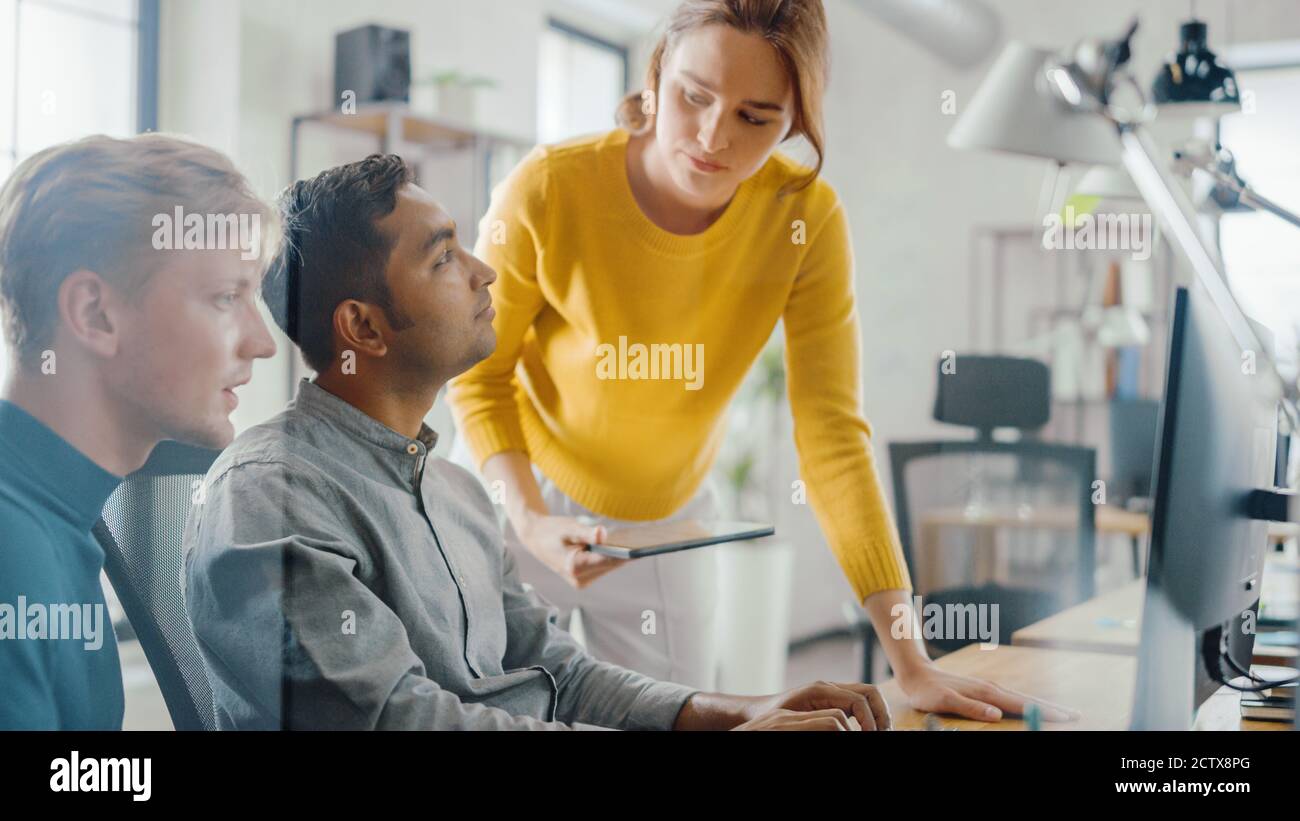Imprenditore di talento che lavora sul suo computer desktop con Project Manager e Team leader in piedi accanto a lui, hanno discussione, trovare il problema Foto Stock