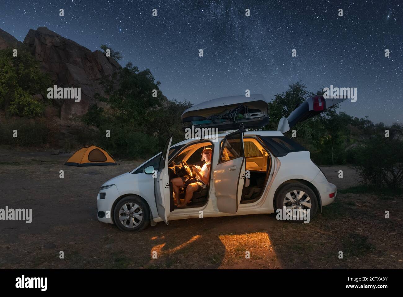 Un viaggiatore esamina una mappa mentre si siede in un'automobile nelle montagne sotto la luce del cielo stellato. Avventura e concetto di viaggio Foto Stock
