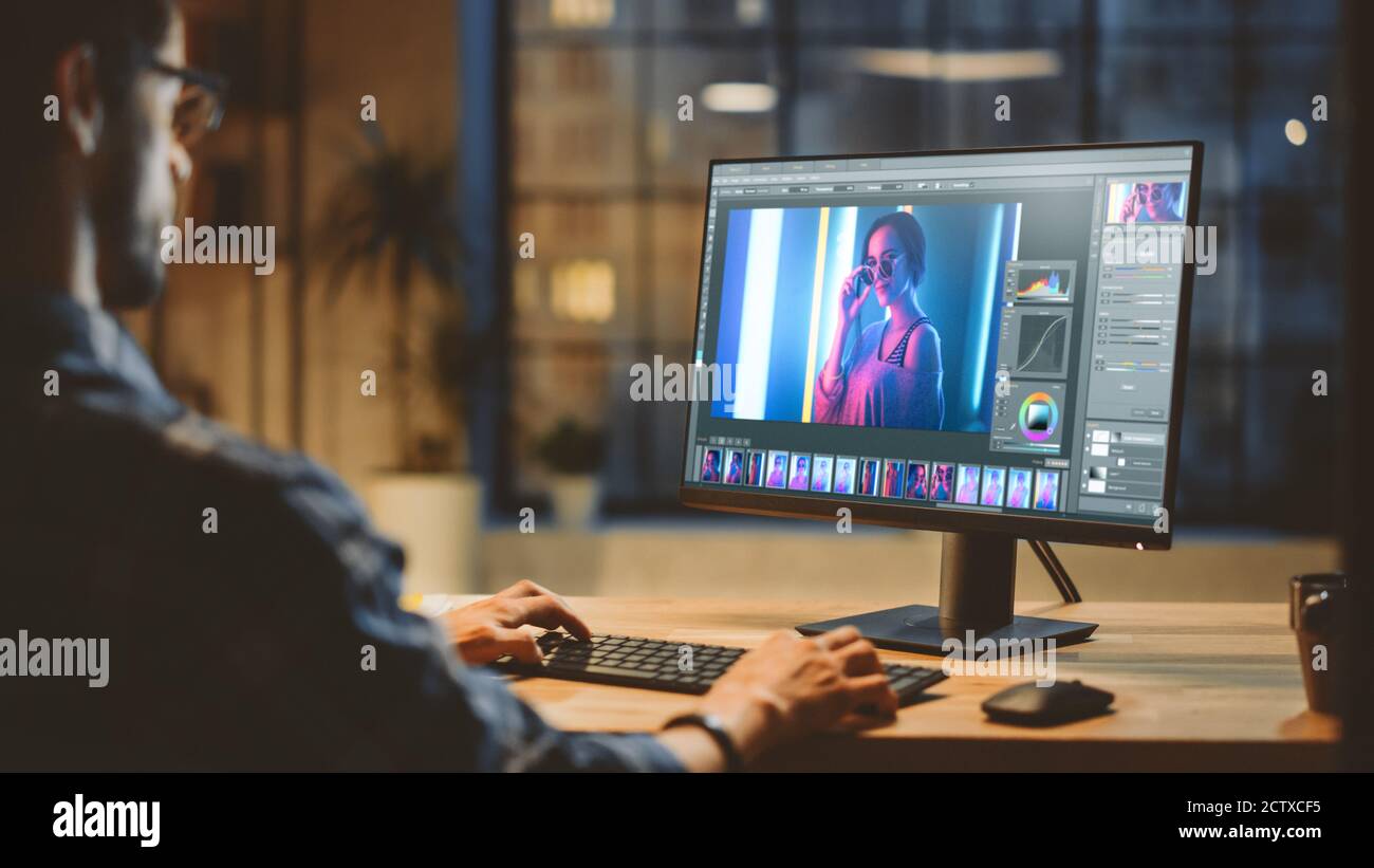 Oltre la spalla: Creative Young Digital Editor lavora nel software di editing fotografico sul suo Personal computer con Big Display. In serata di background Foto Stock
