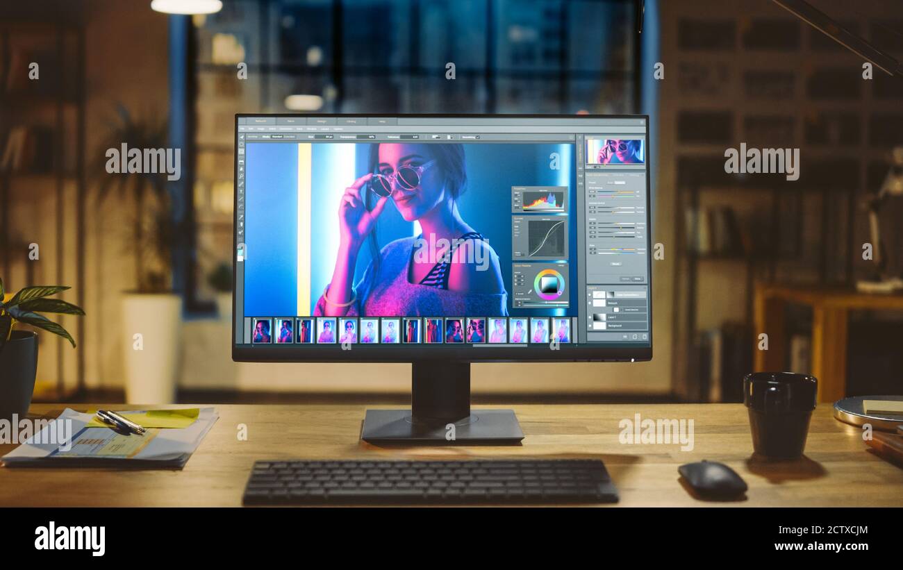 Immagine di un computer desktop nell'ufficio moderno con Monitor che mostra il software di editing fotografico. In background luce calda sera e spazio aperto Foto Stock