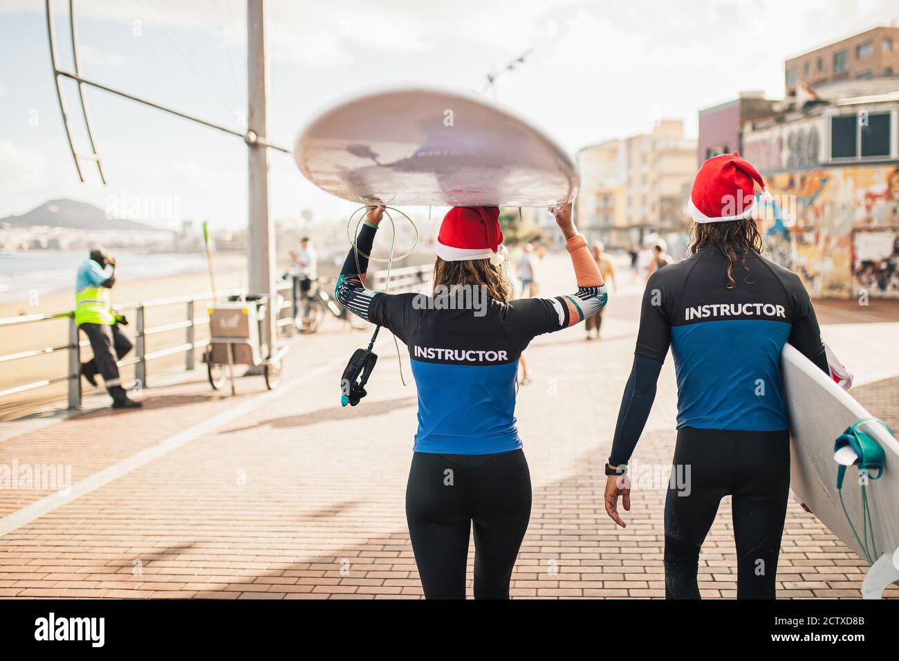 Interessanti gli istruttori di surf giovane a piedi con i loro tavola da surf lungo la passeggiata sul lungomare Foto Stock