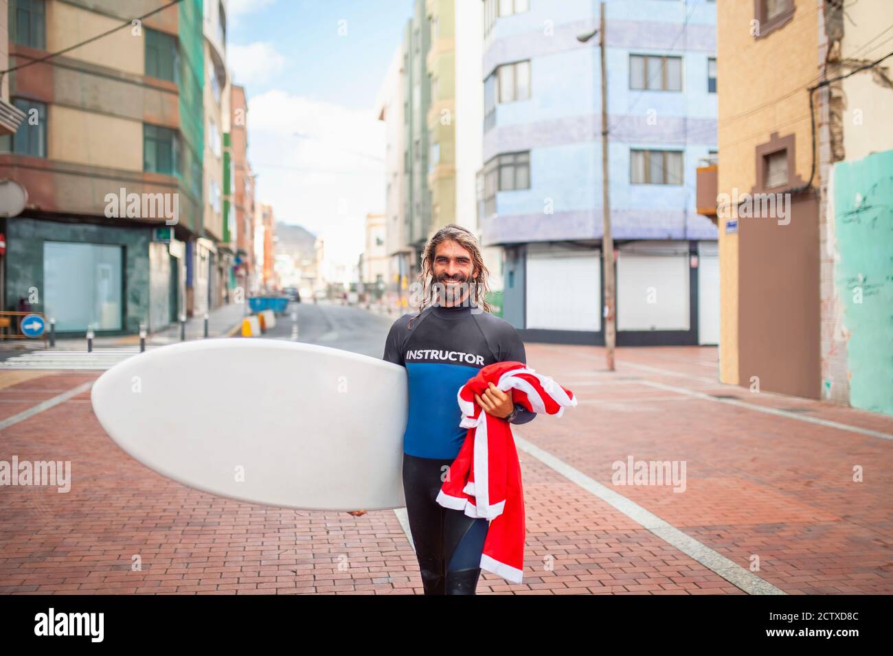 Attraente istruttore di surf uomo che cammina con la sua tavola da surf lungo il lungomare Foto Stock