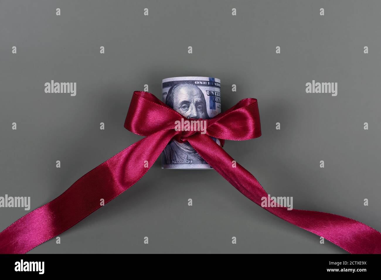 Centinaia di dollari legati con arco rosso su sfondo grigio. Denaro, regalo avvolto in arco rosso e nastro, valuta americana, contanti, successo aziendale, bonus Foto Stock