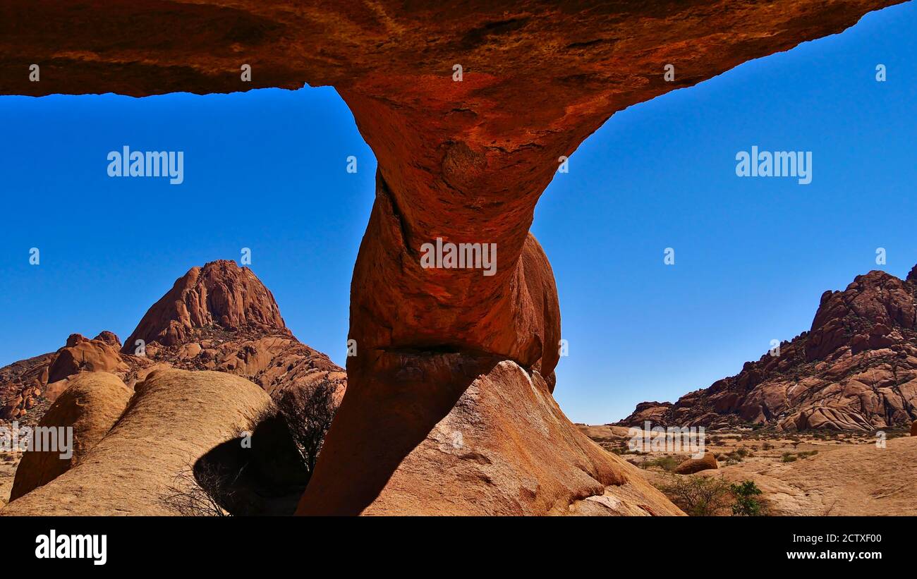 Arco di roccia naturale di colore arancione con rocce arrotondate e montagne sullo sfondo a Spitzkoppe, deserto di Kalahari, Namibia, Africa. Foto Stock